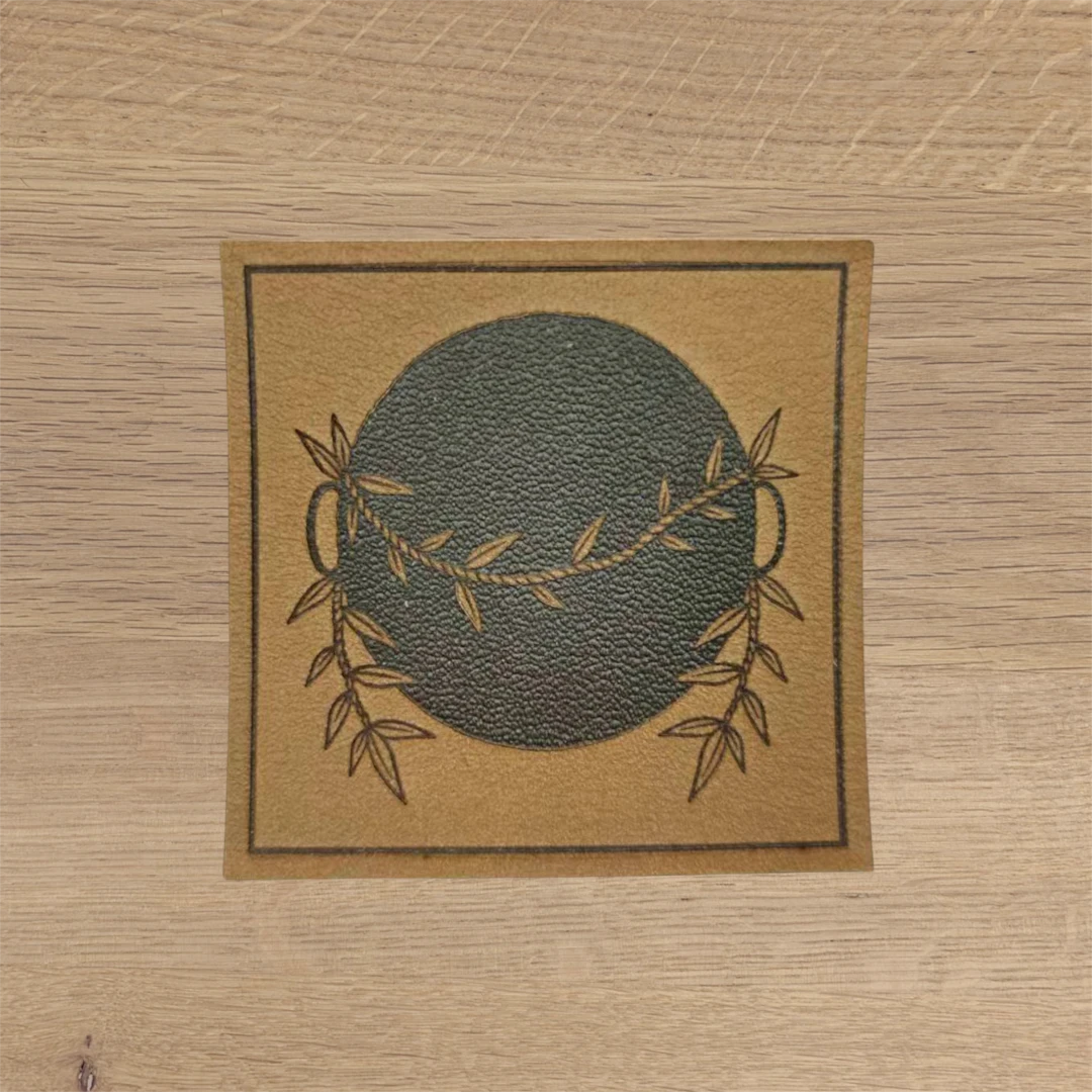 tan square leather patch with engraved laurel wreath design